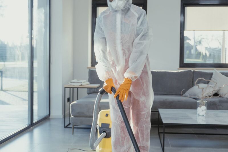Restoration technician in full PPE cleaning a mold-affected area